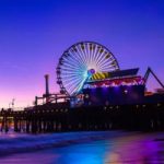 10-Best-Historic-Seaside-Amusement-Parks-In-America---Photo-by-Scott-Trento-(Unsplash) A multi-colored Ferris wheel reflects off the water by the Santa Monica Pier | Photo by Scott Trento, Upsplash