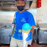 Pacific Park team member, Juaan, serving a cone of bright-blue Cookie Monster ice cream at Scoops