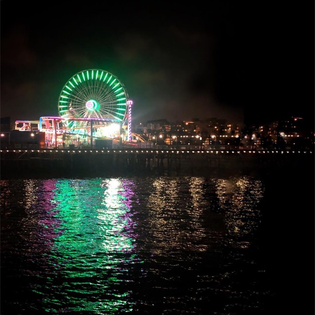 Image of the santa monica pier ferris wheel lit up in green purple and yellow