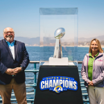 Rams fans stand next to the Vince Lombardi Super Bowl Trophy with views of Santa Monica Beach in the background.