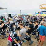 A group of athletes sit on stationary bikes preparing for a fitness event and fundraiser at the Santa Monica Pier.