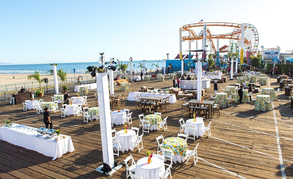 The santa monica pier boardwalk lined with tables and chairs before a larger event.