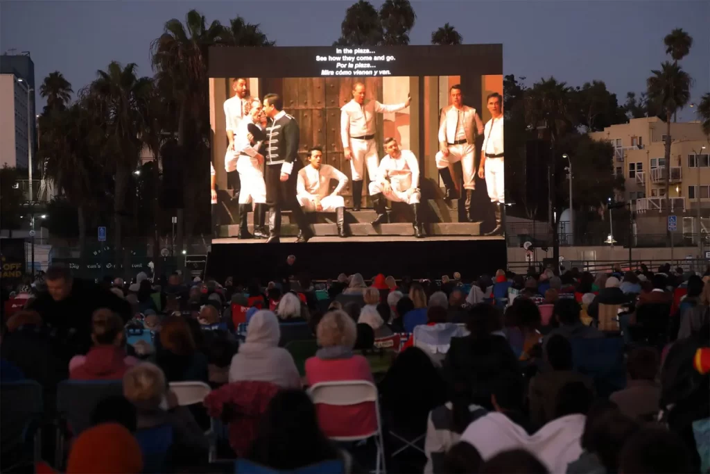Guests sit on beach chairs and picnic blankets while watching a simulcast of the LA Opera on a giant screen atop the Santa Monica Pier