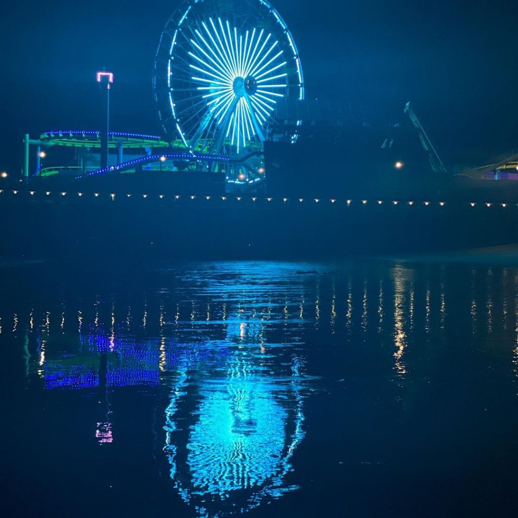 A teal heart illuminated on the Ferris wheel in Santa Monica reflects of the waters around the pier - photo by @curiel_ad