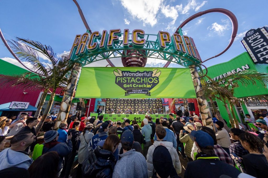A crowd gathered outside a green stage underneath the Pacific Park sign on the Santa Monica Pier