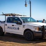 A pick-up truck with surfboards on the top rack and "Police" written on the side photographed at the end of the Santa Monica Pier | Photo by @evcar.pics