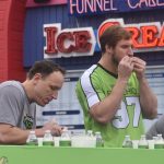Joey Chestnut and Joey Bosa eating Pistachios behind a green table at Pacific Park on the Santa Monica Pier