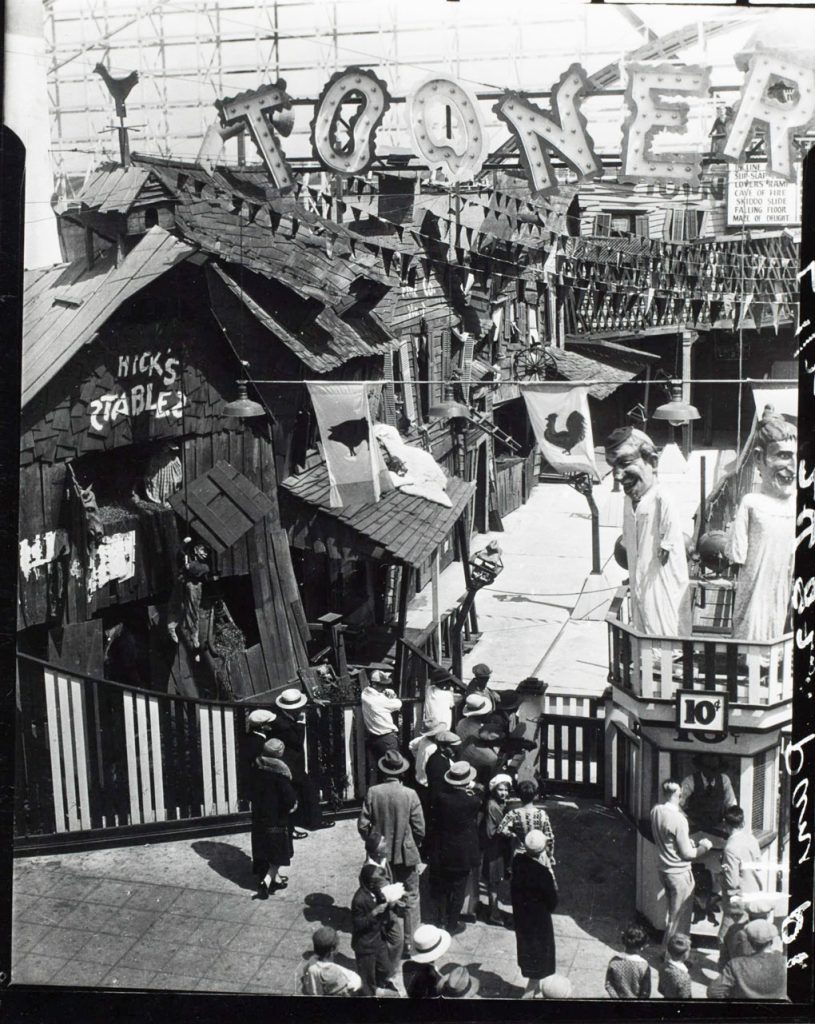  Image of a line of people in front of the Toonerville Fun House on the Ocean Park Pier in Santa Monica, California. Signs on the ride read "cave of fire, skiddo slide, falling floor and maze of delight."